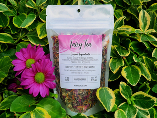 Package of Fairy Tea in with pink label, against a green foliage background with pink flowers 