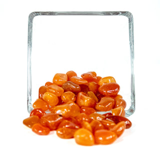 Several dozen orange and red tumbled carnelian pocket stones, in a glass bowl against a white background.