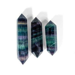 Three double terminated fluorite crystals with points on each end. Each has natural striation of purples, blues and teals. 