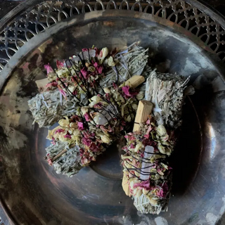 Three cleansing herbal bundles, each with palo santo, dried florals and a clear quartz crystal in a silver bowl.
