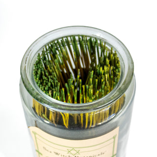 Looking into the top of the glass apothecary jar full of green tipped incense sticks.