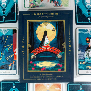 Box of the Tarot of the Divine Deck shows a japanese inspired image of a woman with long hair in a kimono standing on a red bridge, a large full moon is behind her. Several other decks from the card surround the box.