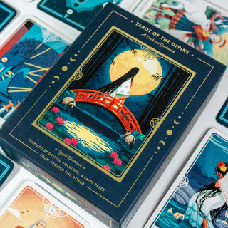 Box of the Tarot of the Divine Deck shows a japanese inspired image of a woman with long hair in a kimono standing on a red bridge, a large full moon is behind her. Several other decks from the card surround the box.