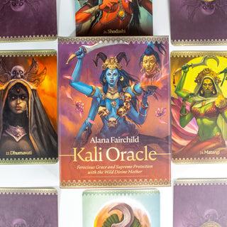 Box of the Kali Oracle Deck by Alana Fairchild. Box is red and purple and shows a blue Kali with multiple arms wearing a necklace of skulls. She holds a blad. There is a severed head to her right. Other cards from the deck surround her.