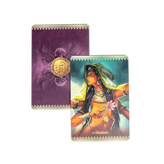 The Shodashi card from the Kali Oracle Deck shows a woman with four arms, she is cloacked and wears armor. A second card behind it shows the back of each card. It is purple with a Hindu symbol in the center and skulls with wings on the top and bottom. 