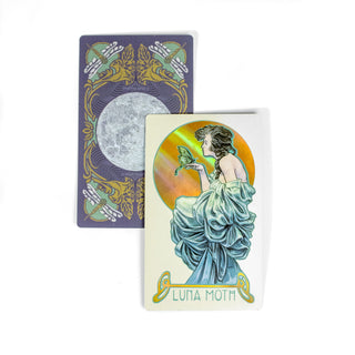 The Luna Moth card from the Dreamscape Oracle deck shows a woman from the side. She is dressed in a draped blue dress and a luna moth rests on her hand. A second guard behind it shows the back of the deck, it is purple with a full moon at the center and dragonflies at each corner.