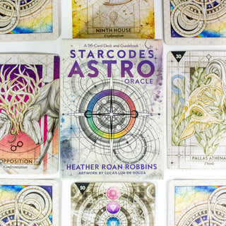 Starcodes Astro Oracle deck box. Has a compass in the center with rainbow band around it and other sacred geometry. Other cards from the deck surround the box