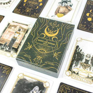 The Magick and Mediums Oracle Deck box is black with golden drawings of crescent moons, crystals and eyes. Other cards from the deck surround it.