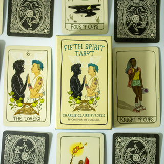 Fifth Spirit Tarot deck box shows two people palm to palm. One is in full color with short blue hair and tattoos, the other is a black outline with stars inside. There are apple twigs with apples below them and rope. Other cards from the deck surround the box.
