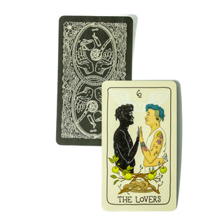 The Lovers card from the Fifth Spirit Tarot deck shows Fifth Spirit TarThe Lovers card from the FIfth Spirit Tarot Deck shows two people palm to palm. One is in full color with short blue hair and tattoos, the other is a black outline with stars inside. A second card behind it shows the back of the cards. It is black white white line drawings of two palms and items representing each of the tarot suits- pentacle, candle, cup and knife.