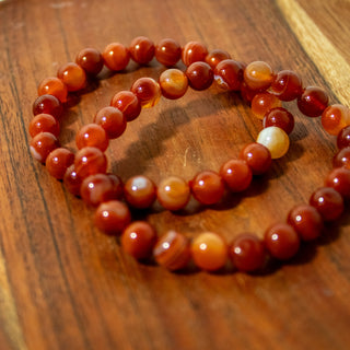 Close up of two carnelian gemstone beaded bracelets. Beads are red and orange. 