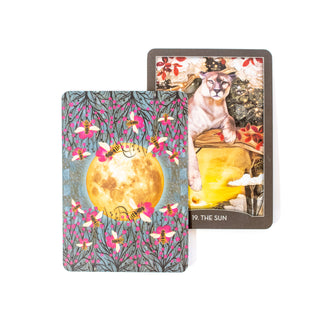 The Sun card from the Guardian of the Night tarot deck shows a leopard in bright sun with red flowers. A second card showing the back of the deck features a full moon with pink flowers and bees.