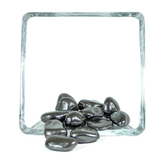 Metallic tumbled hematite pocket stones in a grey color in a glass bowl.