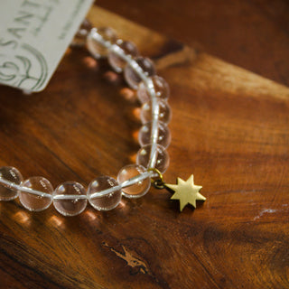 Close up of beaded clear quartz crystal mala bracelet with an eight pointed brass star charm on a wooden background.
