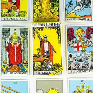 Classic Rider Waite Tarot deck box is yellow with the Magician card image on the front- a man in a red robe holding a wand above his hed. There are several other cards from the deck surrounding the box.