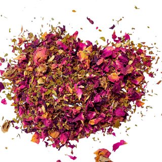 Dried pink flowers and green herbs creating a loose leaf tea on white background.