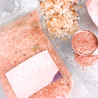 Bag of rose quartz infused Healers Horizon bath salts. Next to bag is bowl of pink salt and chunks of Himalayan sea salt.