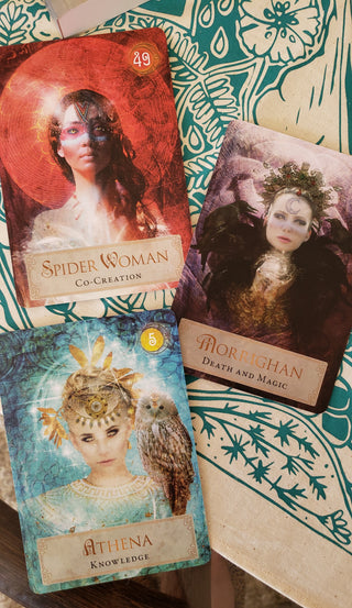 The Spider Woman, Morrigan and Athena cards from the Goddess Power Oracle deck are shown on a teal and beige altar cloth.