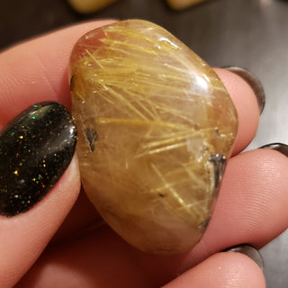 Close up of a rutilated quartz tumbled pocket stone with gold striation.