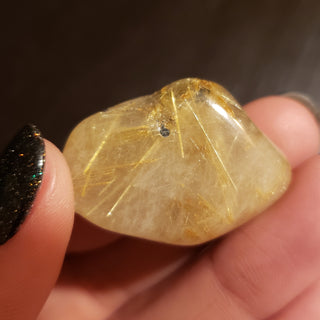 Close up of a rutilated quartz tumbled pocket stone with gold striation. 