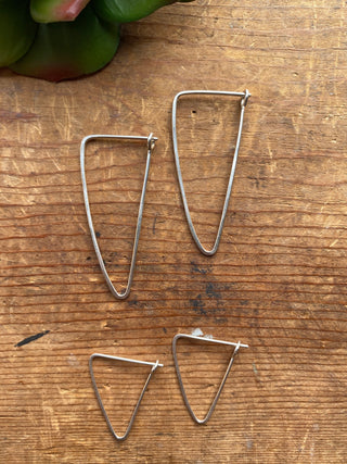 Close up of silver triangular hoop earrings with larger pair at the top and smaller hoop earrings below.