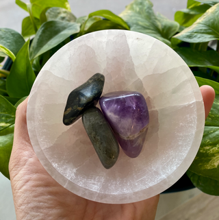 Round selenite bowl held in a palm, with three tumbled crystals inside. Bowl is white with natural variation.