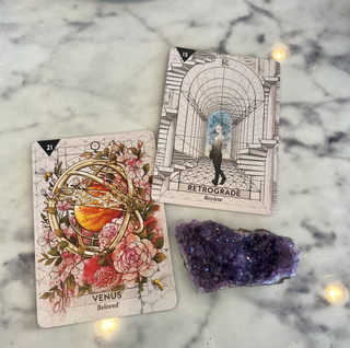 The Venus Beloved card from the Starcodes Astro deck shows the planet surrounded by pink flowers and an open pomegranate. The Retrograde Review card shows a person walking through a long hallway in black and white.