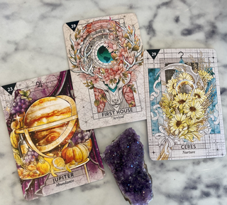 Three cards from the Starcodes Astro deck are shown. Jupiter Abundance card shows the planet on a feast table with food and wine. The First House arrival card shows a stag with flowers in its horns. The Ceres Nuture card shows a skythe surrounded by yellow flowers.