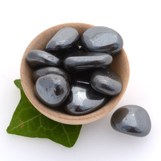 Metallic tumbled hematite pocket stones in a grey color in a wooden bowl.