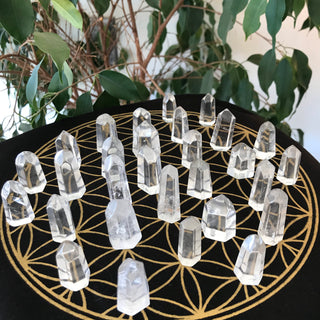 Several mini clear quartz generators shown on a black crystal grid cloth with gold sacred geometry. 