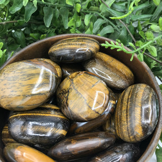 Bowl of tigers eye palm stones all soap shaped with natural variations of colors of gold and brown and striping